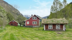 A red wooden house with a thatched roof, surrounded by a grassy field and mountains in the background. - 3 bedroom beautiful home in Vik i sogn (Vik i sogn)
