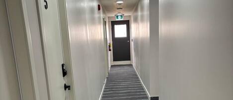 A hallway with a carpeted floor, white walls, and a door marked with the number 5.