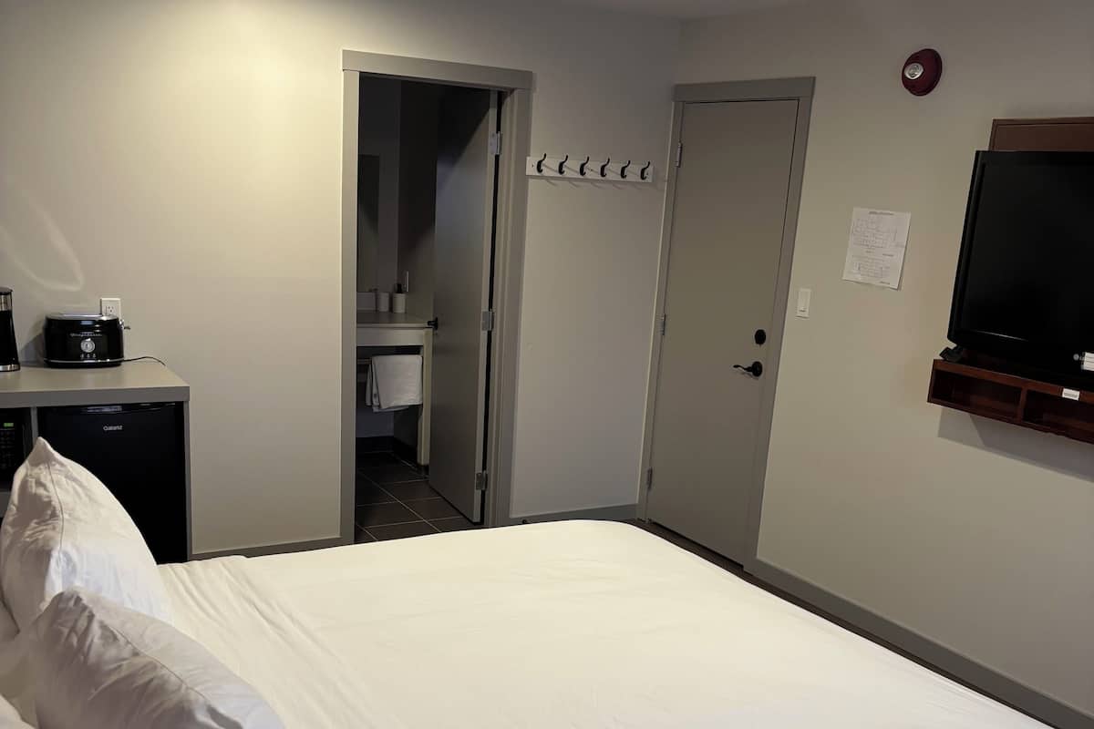 A hotel room with a bed, a desk with a coffee maker, a television, and a door leading to a bathroom.