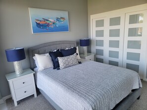 Un dormitorio con una cama, dos mesitas de noche, una lámpara, un cuadro y una puerta con paneles de vidrio esmerilado.
