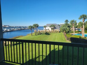 A marina with boats, a grassy area with palm trees, and a building with a grey roof.