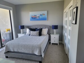 A bedroom with a bed, two bedside tables with lamps, a painting on the wall, and a sliding door.