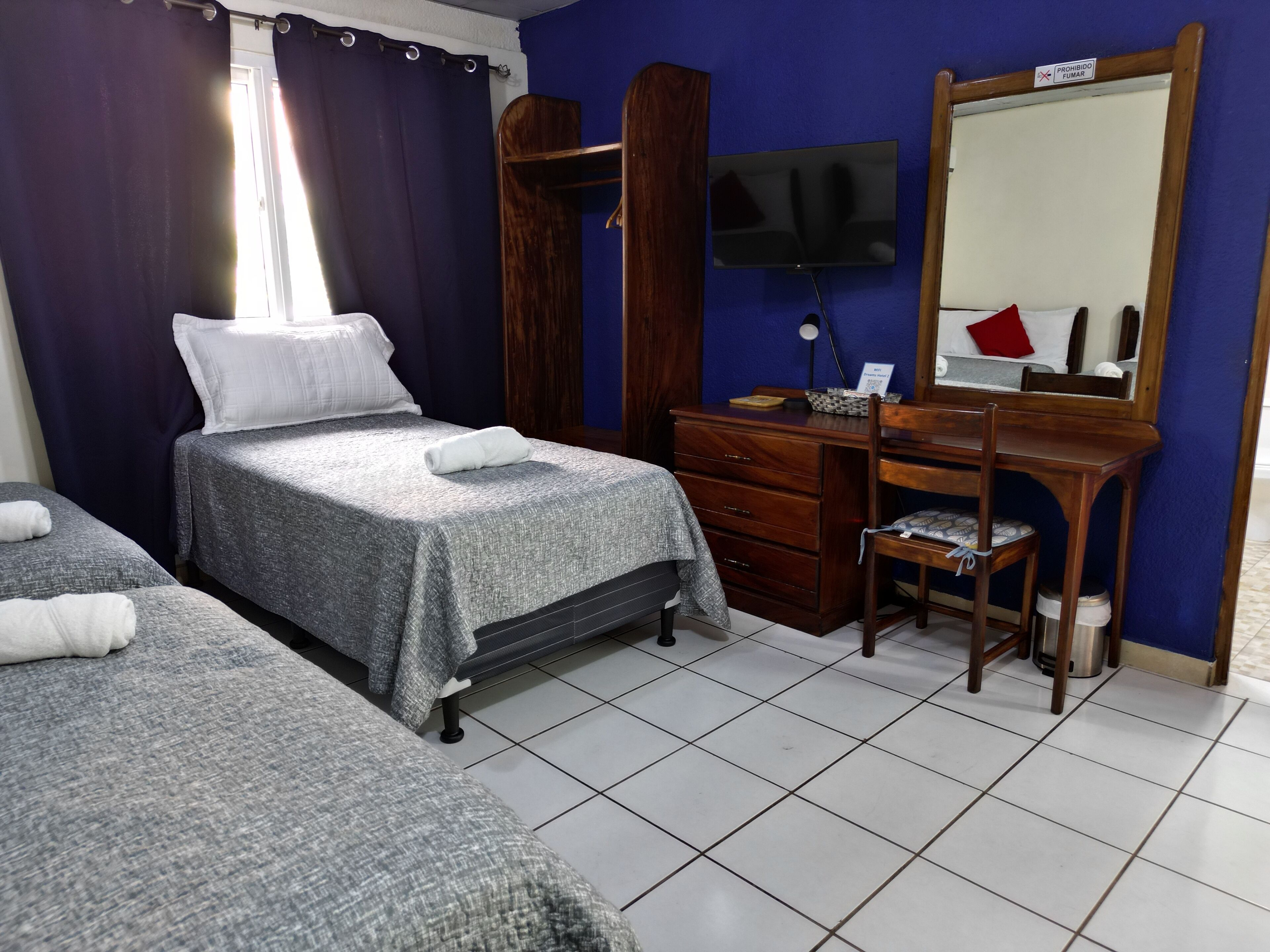 Ein Hotelzimmer mit zwei Betten, einem hölzernen Schminktisch, einem Schreibtisch mit Stuhl, einem an der Wand montierten Fernseher und einem Spiegel über dem Schminktisch.