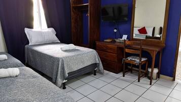 Une chambre d’hôtel avec deux lits, une commode en bois, un bureau avec une chaise, un téléviseur fixé au mur et un miroir au-dessus de la commode.