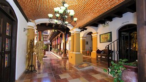 A spacious hallway with a tiled floor, a chandelier, and columns. - HOTEL PLAZA SAN CRISTOBAL INN (San Cristóbal de las Casas)