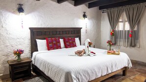A bedroom with a wooden bed frame, white bedding, a nightstand with a vase of flowers, and a window with curtains. - HOTEL PLAZA SAN CRISTOBAL INN (San Cristóbal de las Casas)