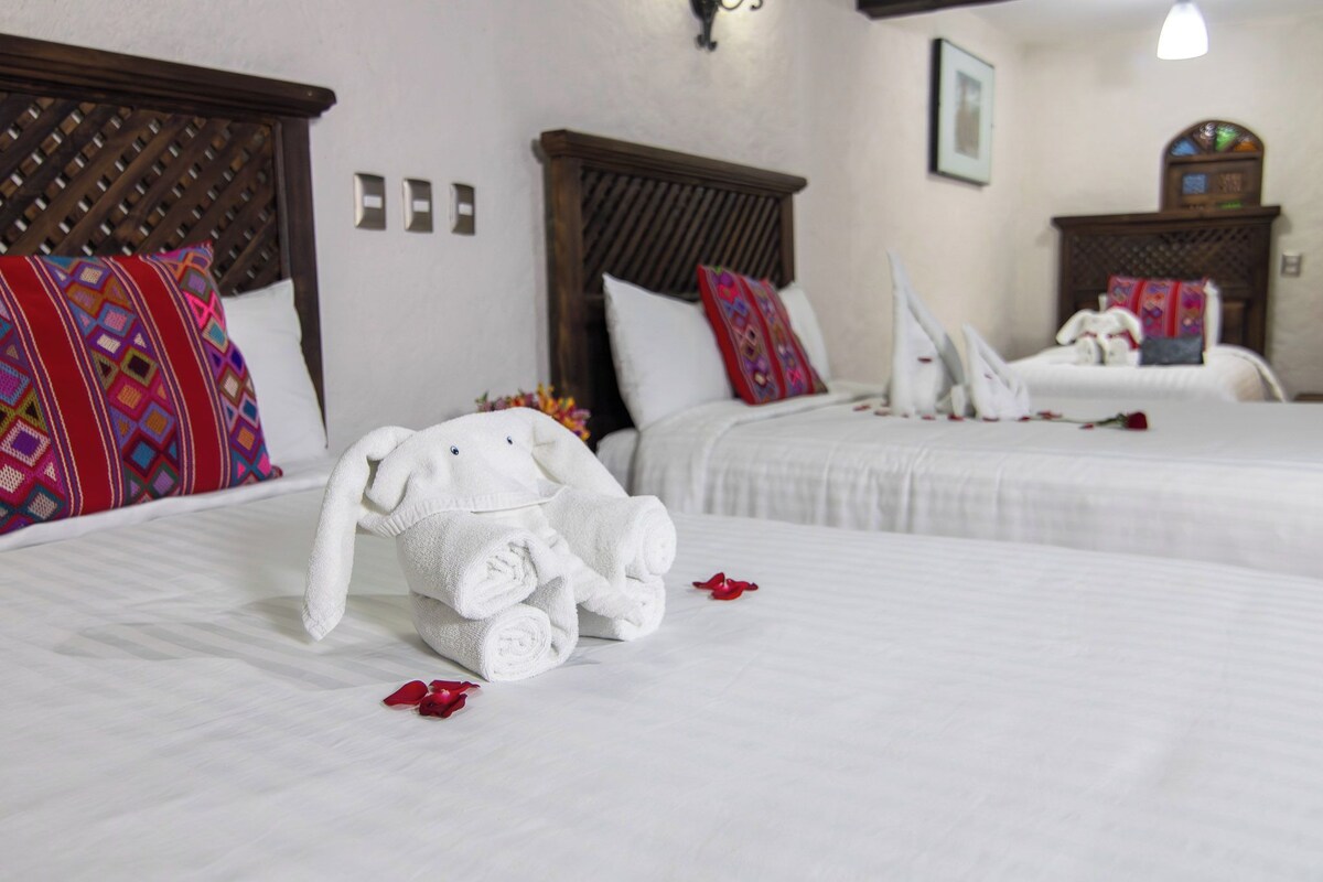 Habitación de hotel con dos camas, cada una con cabecero de madera y ropa de cama blanca.