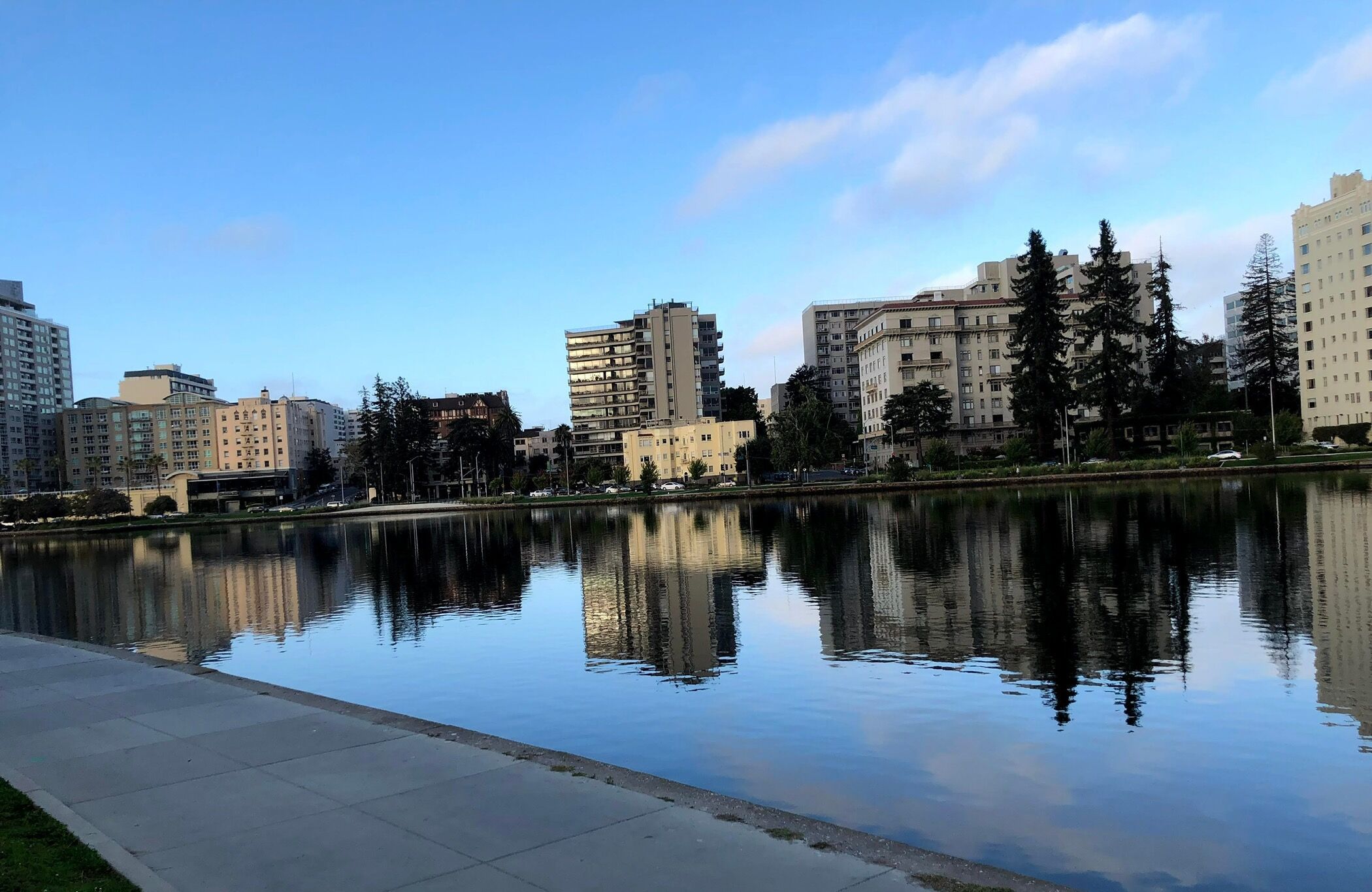 Un lac urbain paisible, dont les eaux reflètent les bâtiments environnants, et qui est bordé de diverses constructions résidentielles et commerciales.