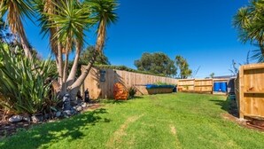 A backyard with a wooden fence, a blue barrel, and a small shed.