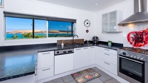 A modern kitchen with white cabinets, a black countertop, a stove, and a window with a view of the landscape.
