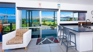 A modern kitchen with a bar area, large sliding glass doors leading to a balcony with a view of the sea and hills.