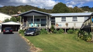 A residential property with a garage, two cars parked in front, a covered porch, and a grassy yard.