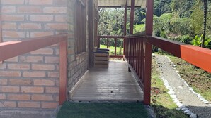A covered outdoor area with a brick wall, a wooden bench, and a stone pathway leading to a lush green landscape. - Quindanna  (Cosanga)