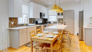 A modern kitchen with white cabinets, a wooden dining table set for four, and a stainless steel refrigerator. -  Large 3BR Pet-Friendly Apt w/Free Parking Near Red Line-Downtown Boston 82 (Boston)