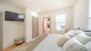 A bedroom with a bed, a TV mounted on the wall, a window, and a door leading to a bathroom. -  Large 3BR Pet-Friendly Apt w/Free Parking Near Red Line-Downtown Boston 82 (Boston)