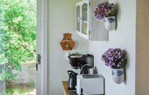 A kitchen with a toaster, kettle, and pots on the counter. There are two wall-mounted flower pots with purple flowers. A wooden decorative piece hangs on the wall. - 4 bedroom nice home in Mörbylånga (Mörbylånga)
