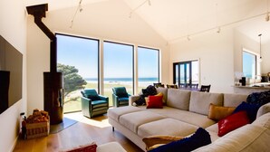Een ruime woonkamer met een grote bank, een open haard en uitzicht op het strand.