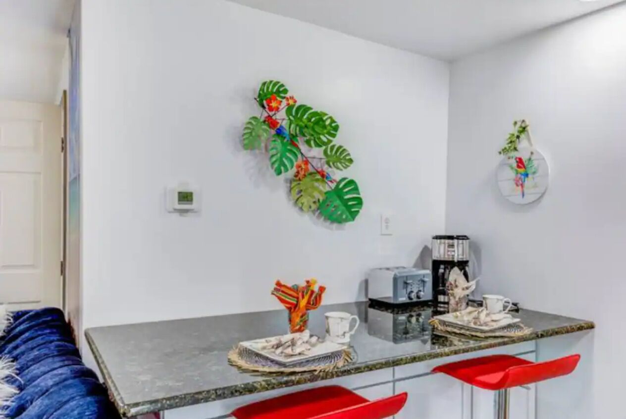 Une cuisine moderne avec un plan de travail en marbre, des tabourets de bar rouges et des œuvres d’art décoratives sur les murs.
