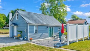A small, single-story house with a metal roof, a front door, and a small porch area with a bench and potted plants. - Cozy stylish home near Hershey park and so many (Campbelltown)