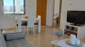 Un salon moderne comprenant un canapé, une table à manger, des chaises, un téléviseur et une vue sur les montagnes par une fenêtre.