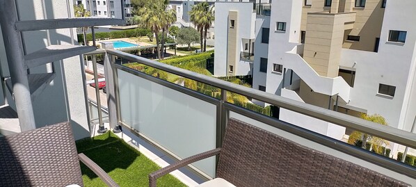 Un balcón con vista a una piscina, edificios cercanos y un césped bien cuidado.