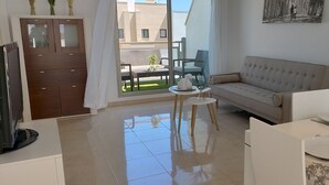 Un salon moderne avec un canapé, une table à manger avec de l’assiette et des verres, un téléviseur et une vue sur le balcon extérieur.
