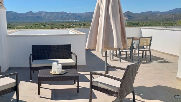 Une terrasse sur le toit, meublée de mobilier en osier, avec une table décorée de bougies et une vue sur les montagnes.