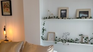 Un salon comprenant un canapé, une table avec une lampe et des étagères ornées de tableaux encadrés et de plantes.