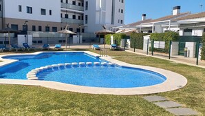 Une piscine de forme circulaire, entourée de pelouse et de chaises longues.