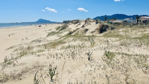 Une plage avec des dunes, un ciel dégagé et des montagnes à l’horizon.
