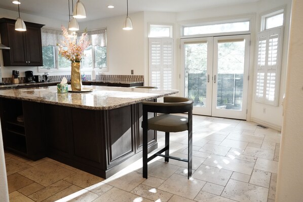 A modern kitchen with dark cabinetry, a marble countertop, and a central island. There are two bar stools and a vase with flowers on the island.