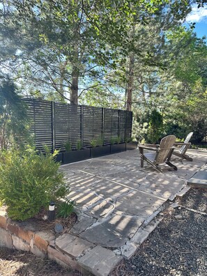 A patio area with stone flooring, a black privacy fence, and two Adirondack chairs.