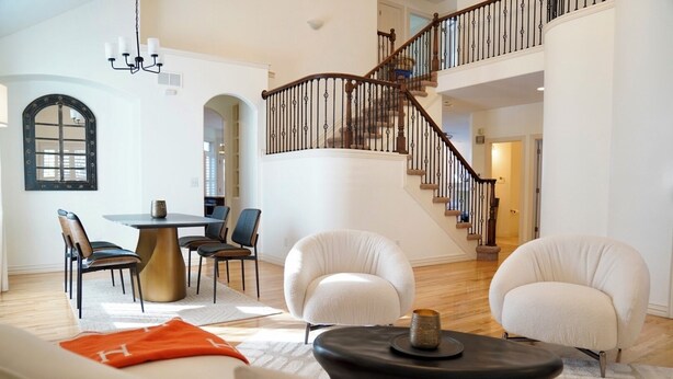 Ein geräumiges Wohnzimmer mit hoher Decke, einer Treppe mit Holzwand und einem Essbereich mit rundem Tisch und Stühlen.