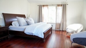 Ein Schlafzimmer mit einem hölzernen Bett, einem Nachttisch, einem Sessel und einem Fenster mit Vorhängen.