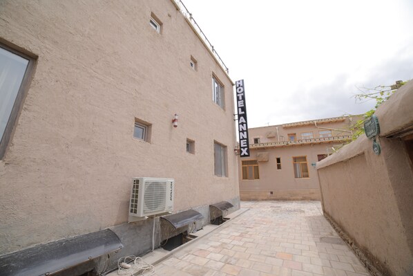 A building with a sign reading "HOTEL AVALON EX." It has a beige exterior, multiple windows, and a tiled courtyard.