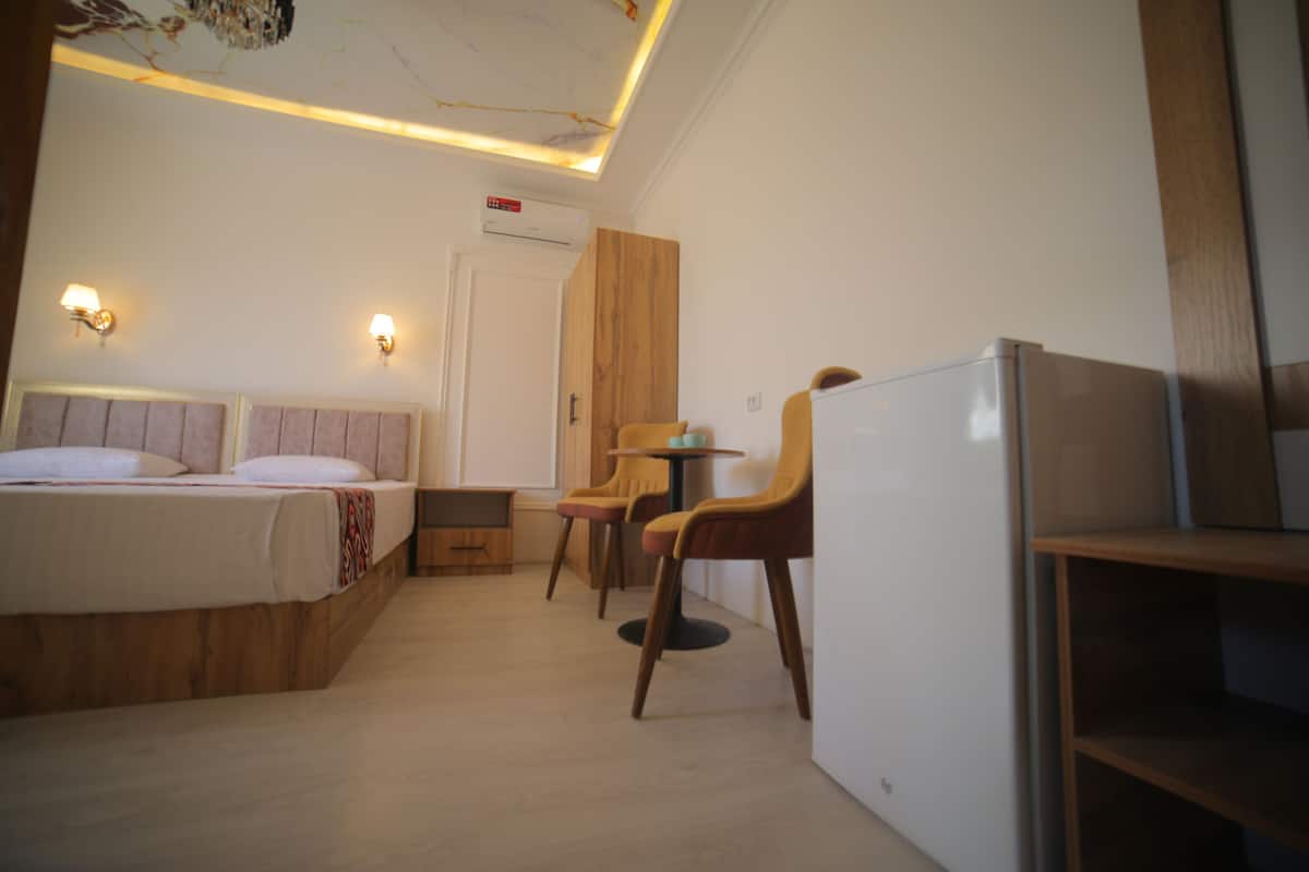 A hotel room with a bed, a desk, two chairs, a small table, and a refrigerator.