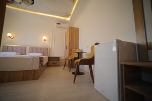 Habitación de hotel con cama, escritorio, dos sillas, una mesita y un refrigerador.