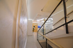 Un interior moderno con barandilla de vidrio, una escalera y vistas a una habitación con televisor.