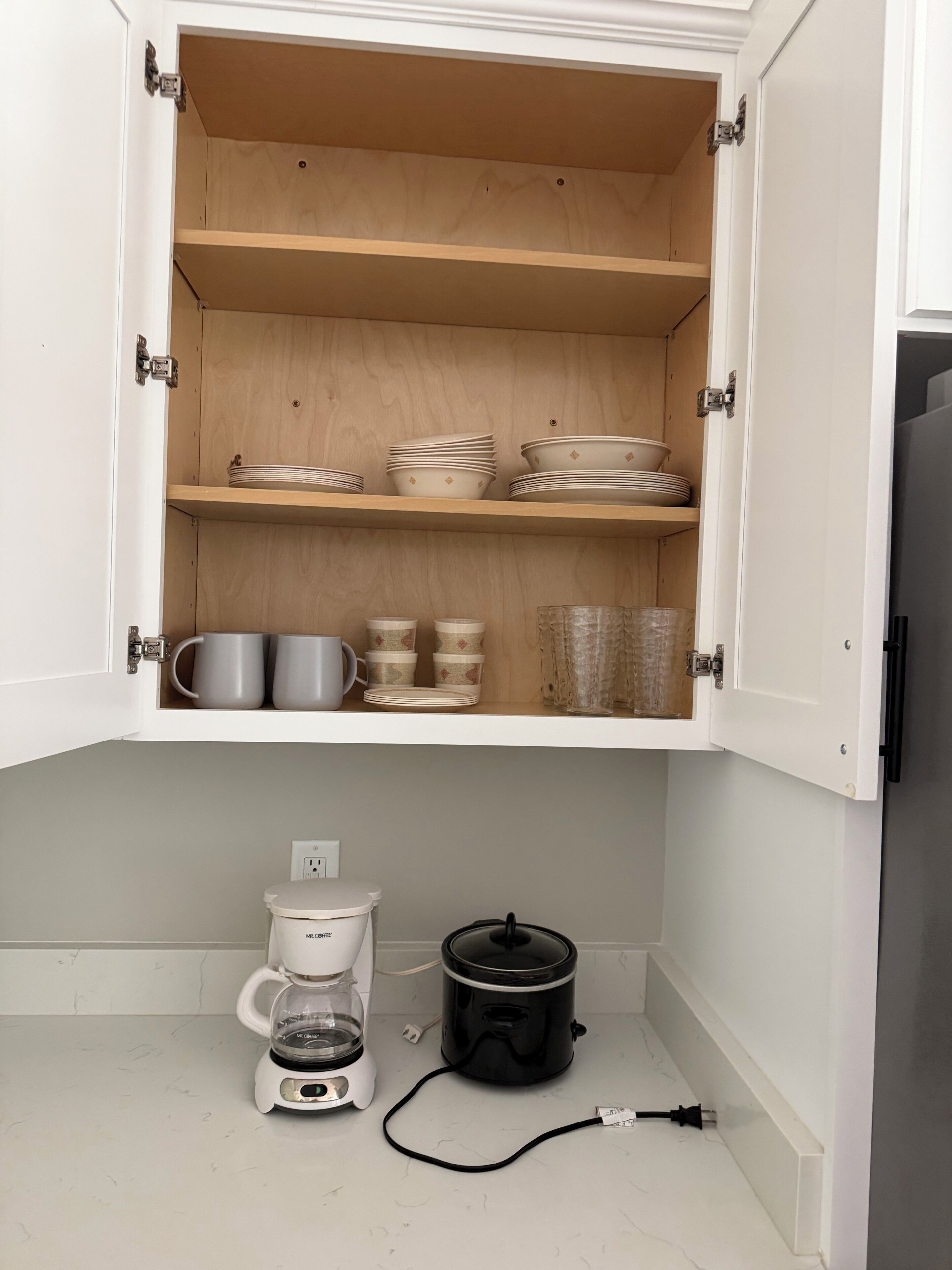 Een keuken met open kastjes waar servies, kopjes en een koffiezetapparaat staan.