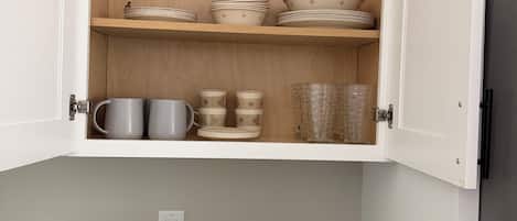 Cozinha com armários abertos exibindo louças, xícaras e uma cafeteira.