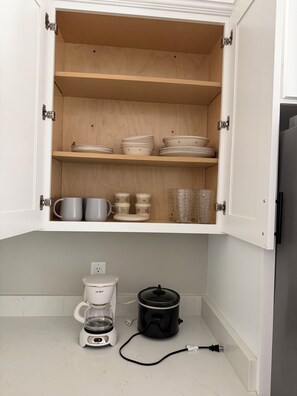 A kitchen with open cabinets displaying dishes, cups, and a coffee maker.