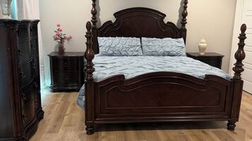 Een slaapkamer met een bed met houten baldakijn, een dressoir, een nachtkastje en een plafondventilator.