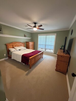Un dormitorio con cama, cómoda, ventilador de techo y ventana con persianas.
