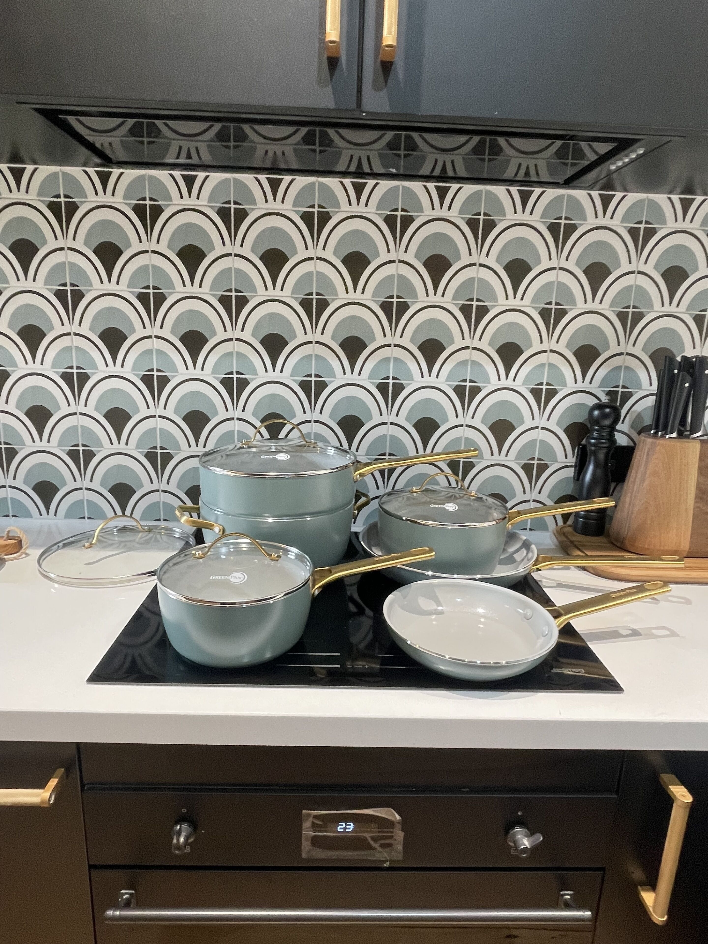 A kitchen with a modern design, featuring a black countertop, a patterned backsplash, and a set of pots and pans with gold handles.