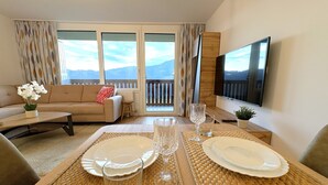 Un comedor con una mesa dispuesta para dos personas, un sofá y un televisor en una habitación con vista a un balcón.