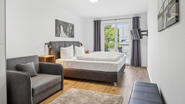 A modern bedroom with a bed, a sofa, a desk, and a large window with curtains. - Pet friendly apartment in Putbus with sauna (Putbus)