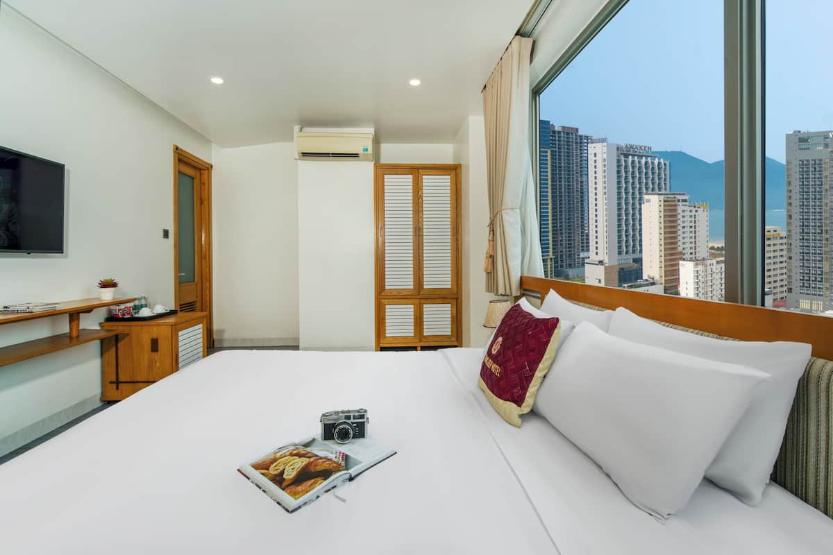 Une chambre d’hôtel équipée d’un lit, d’une télévision, d’un bureau et d’une fenêtre donnant sur la ville.