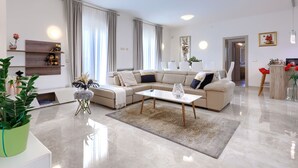 Ein modernes Wohnzimmer mit einem beigen Sofa, einem Couchtisch und einem Essbereich mit einem weißen Tisch und Stühlen.