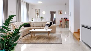 Ein modernes Wohnzimmer mit einem beigen Sofa, einem Couchtisch und einem Essbereich im Hintergrund.
