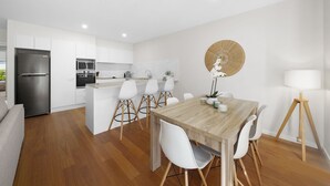 A modern kitchen with white cabinets, a stainless steel refrigerator, and a wooden dining table with white chairs. - Spacious 4BR w/ Water Views (Port Macquarie)